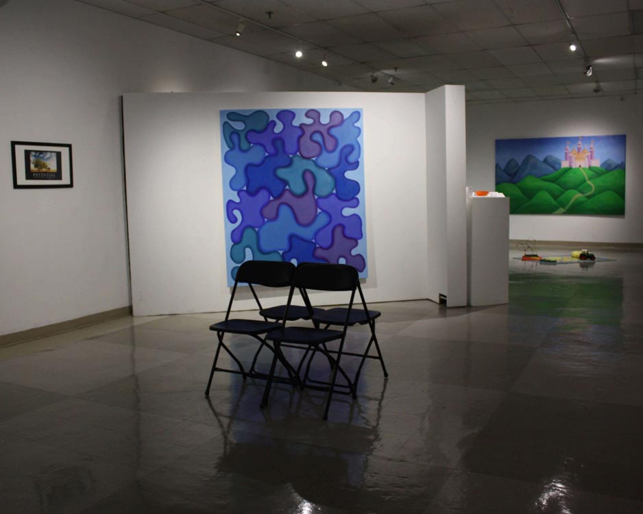 perspective of gallery, foldable chairs are in the center of the room with a blue amorphous painting and smaller posters on the walls