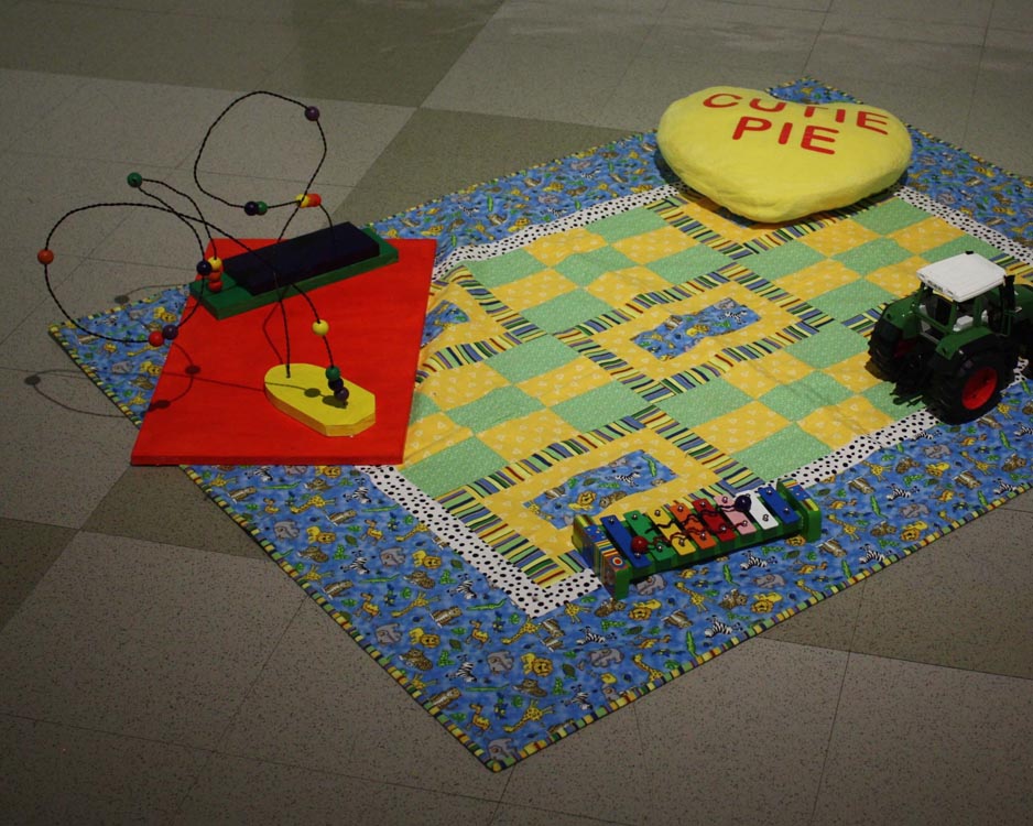 childish blanket with heart shaped pillow, toy truck, xylophone, and wooden bead and wire sculpture